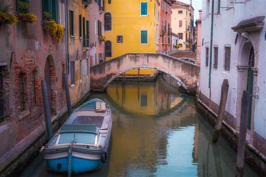Venice canal with a small boat and arched bridge between colorful buildings