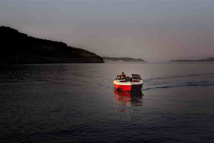 Small red boat moving across calm water at twilight