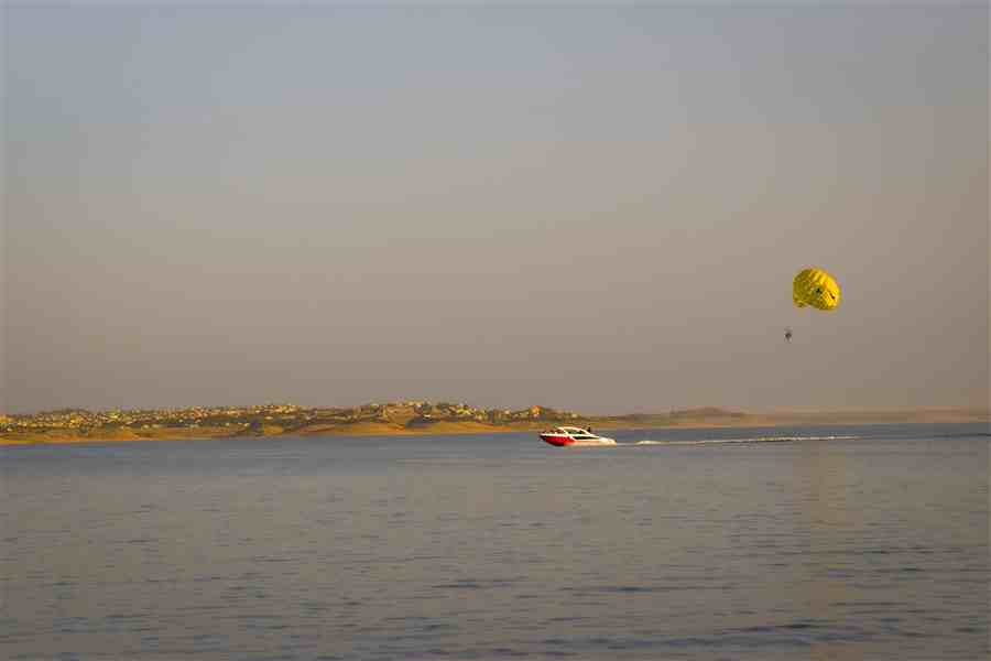 Parasail and speedboat crossing open water in evening light