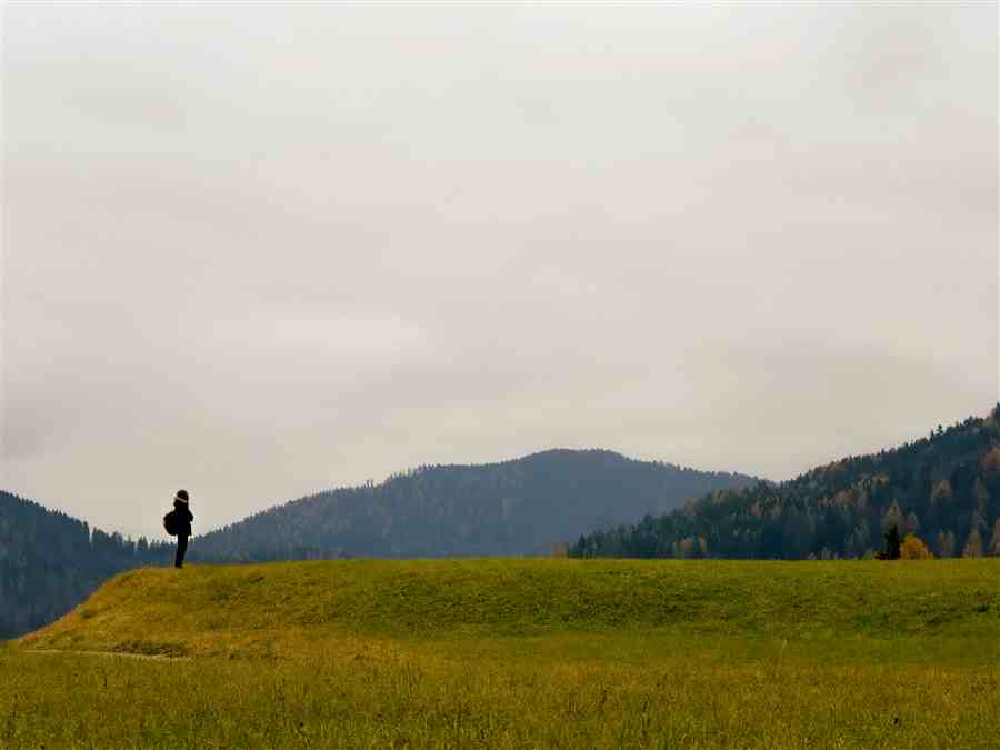 Single figure standing on a grassy ridge beneath distant hills