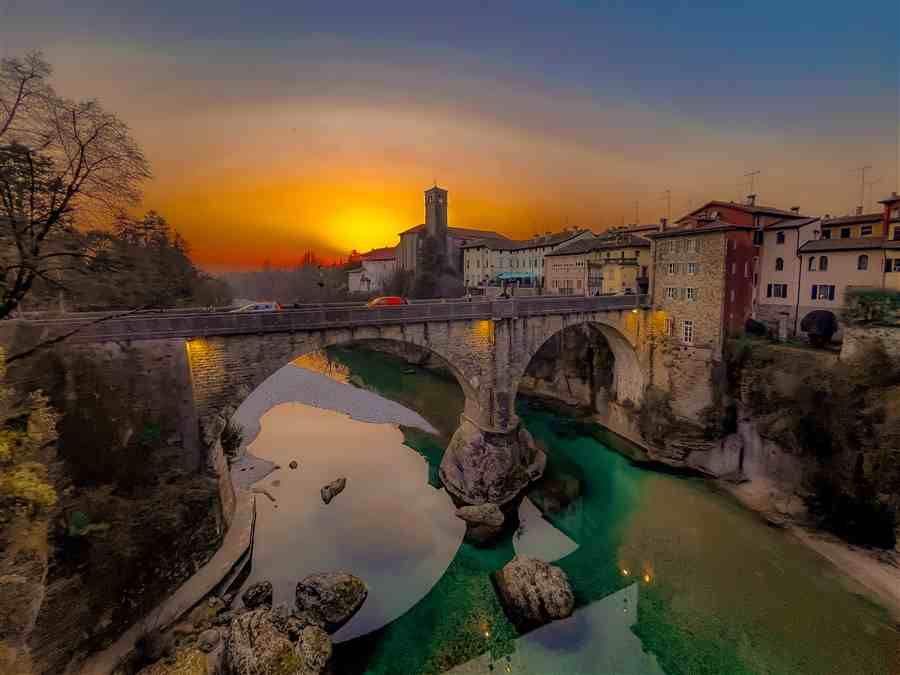 Sun setting behind a stone bridge over vivid green water