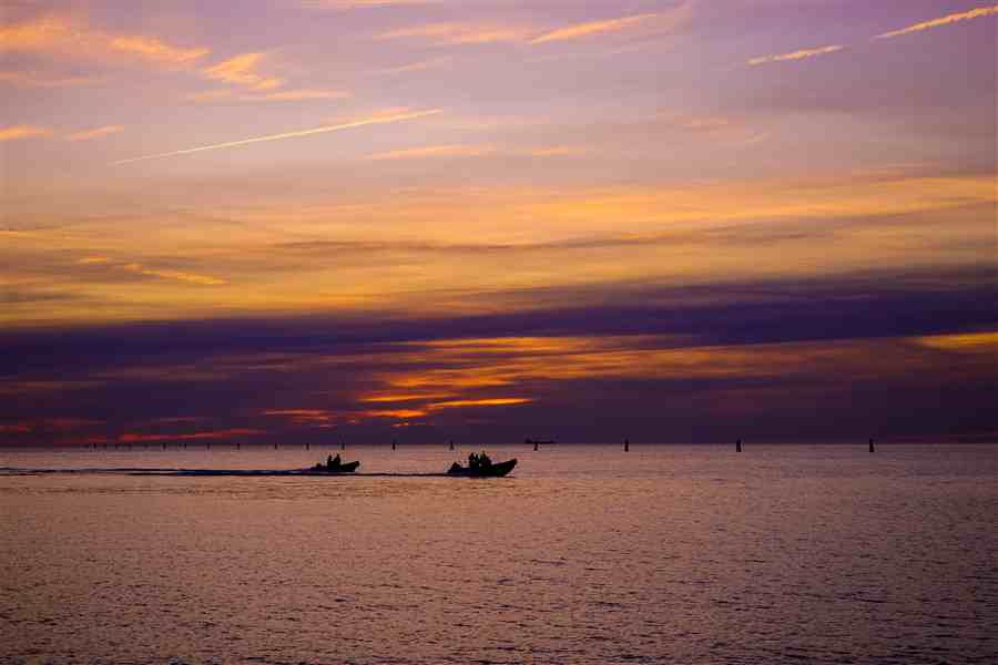 Sunset over open water with boats in silhouette